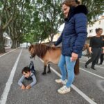 Un enfant allongé au sol près d'un poney brun et près de lui, Lou, la responsable d'Agapé cheval médiation