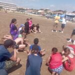 Les jeunes assis sur le sable écoutent les consignes des éducateurs