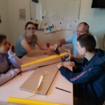 3 jeunes avec un parrain du club d'aéromodélisme autour d'une table construisent un modèle d'avion