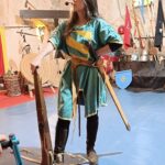 Une animatrice en tenu d'époque avec une épée, tient une arbalette