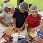 Trois enfants, charlotte sur la tête, autour d'une table, en atelier cuisine