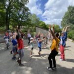 Enfants et animateurs, les bras levés sur un terrain de basket-ball