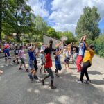 Enfants et animateurs, les bras levés sur un terrain de basket-ball