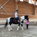 Un jeune sur un cheval avec une autre jeune qui tient la bride du cheval