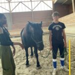 Un jeune tient un cheval par la bride. A ses côtés une animatrice