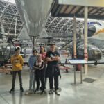 5 jeunes dans le hangar posent devant divers modèles d'avions et hélicoptères