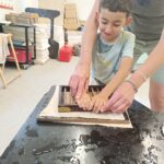 Un jeune confectionne une feuille en papier avec l'aide de l'animatrice