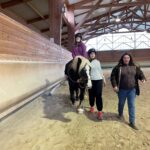 Une jeune sur un cheval, une autre jeune tient la longe et l'encadrante les accompagne