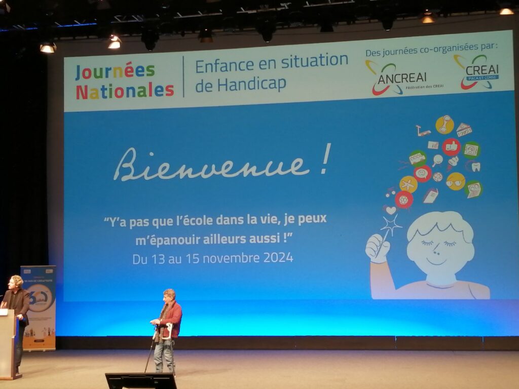 Dans la grande salle, deux personnes sur scène et un écran géant sur lequel est inscrit : Bienvenue : "Y a pas que l'école dans la vie, je peux m'épanouir ailleurs aussi ! " - du 13 au 15 novembre 2024