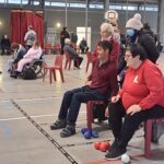 Dans le gymnase, des joueurs durant la compétition de boccia, encouragés par des spectateurs